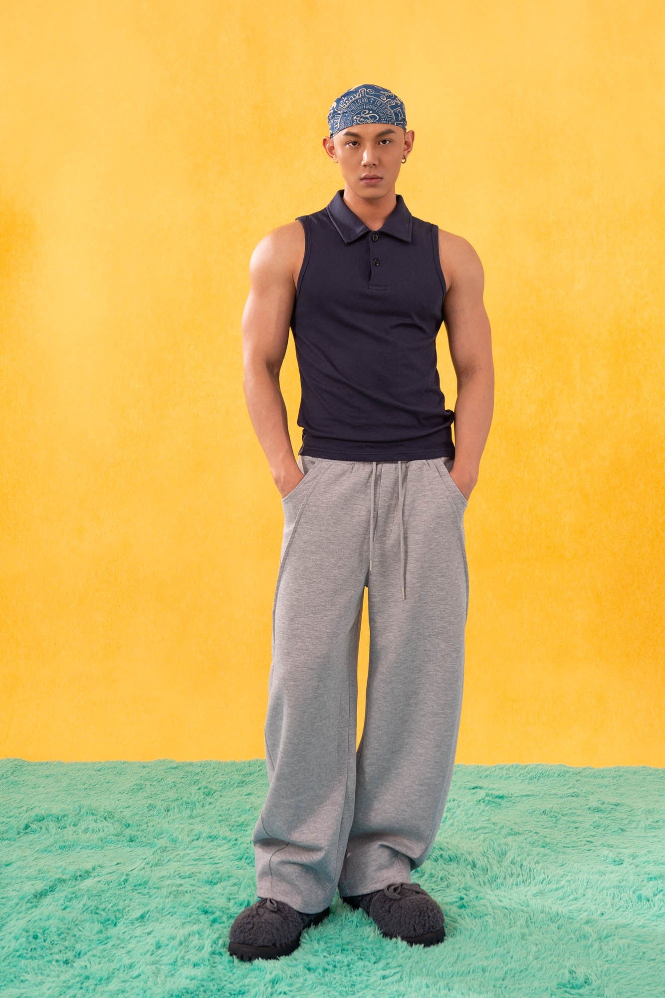 Male model wearing heather gray slanted spliced wide-leg sweatpants with navy tank top and casual streetwear styling