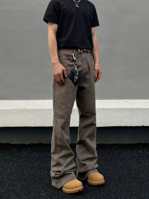 Front full-body view of taupe washed loose straight-leg stacked denim jeans styled with a black T-shirt and waist chain