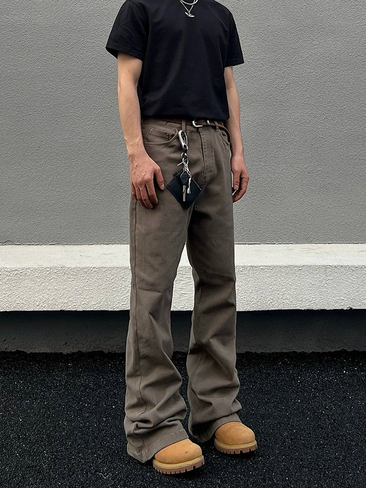 Front full-body view of taupe washed loose straight-leg stacked denim jeans styled with a black T-shirt and waist chain