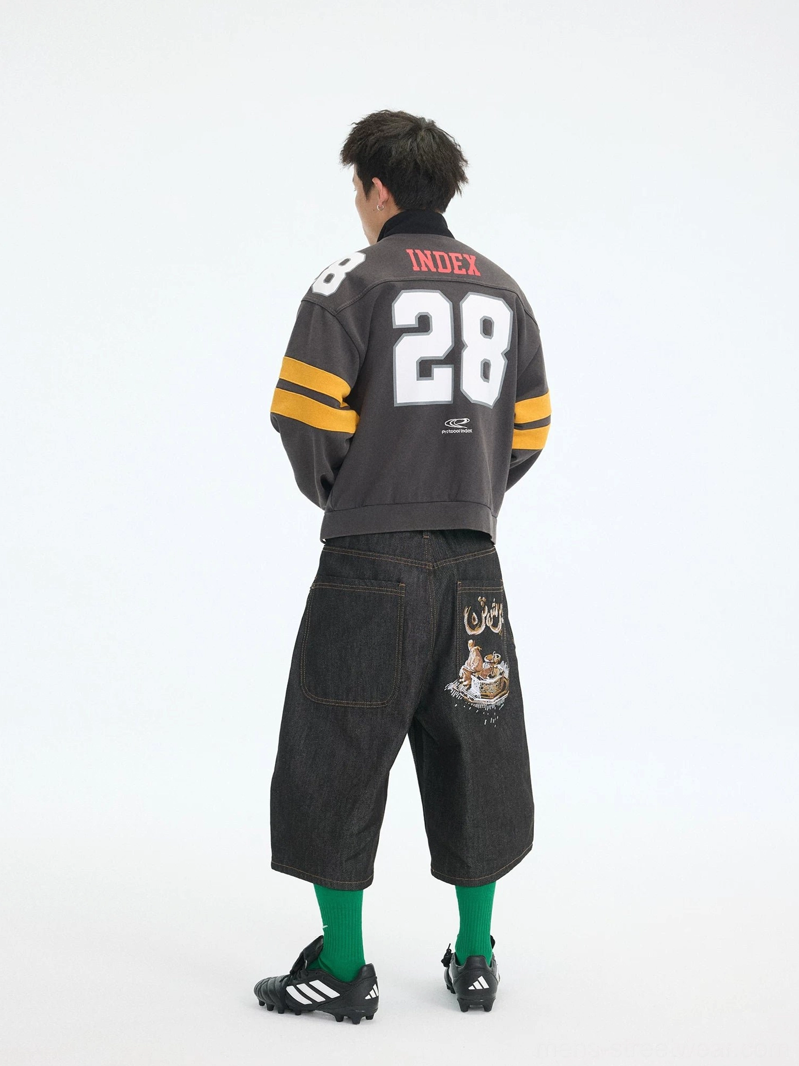 Charcoal gray cropped football streetwear jacket back view with large 28 print and yellow striped sleeves styled with black cropped pants