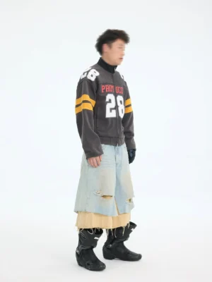 Side view of charcoal gray cropped football jacket with yellow varsity sleeve stripes styled with layered distressed denim and black boots