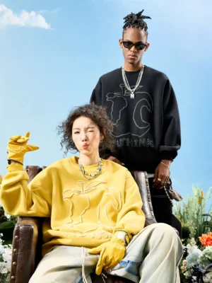 Two-tone oversized embroidered crewneck sweatshirts styled on male and female models in an outdoor flower field, showcasing abstract raised line-art streetwear details
