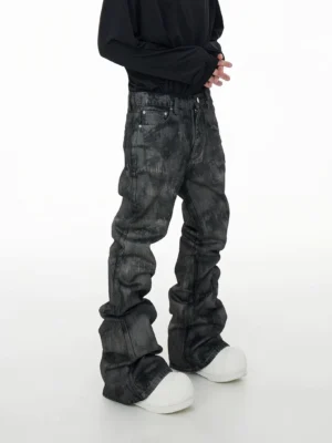 Side view of acid wash coated stacked denim jeans showing the oversized folded leg silhouette, side seams, and faded gray-black finish