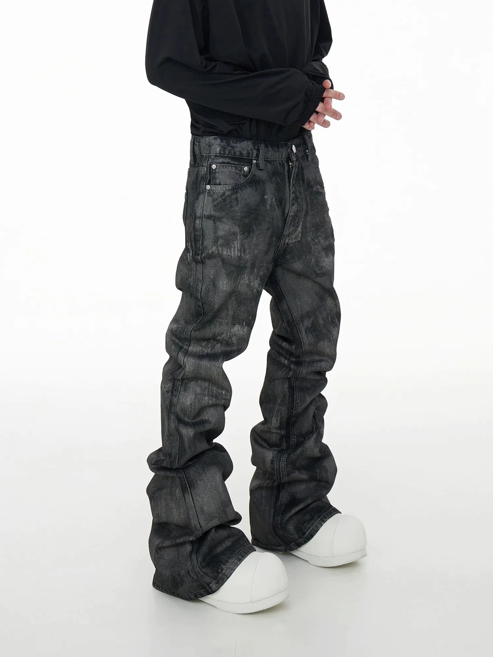 Side view of acid wash coated stacked denim jeans showing the oversized folded leg silhouette, side seams, and faded gray-black finish