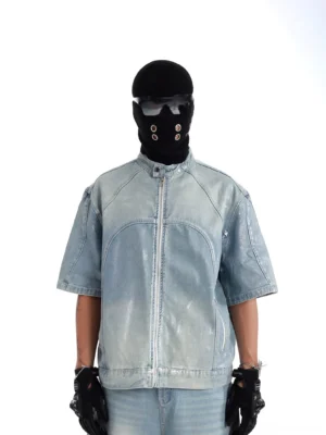 Front view of a faded blue acid wash short sleeve moto denim jacket with stand collar, full zip closure and structured chest panel seams