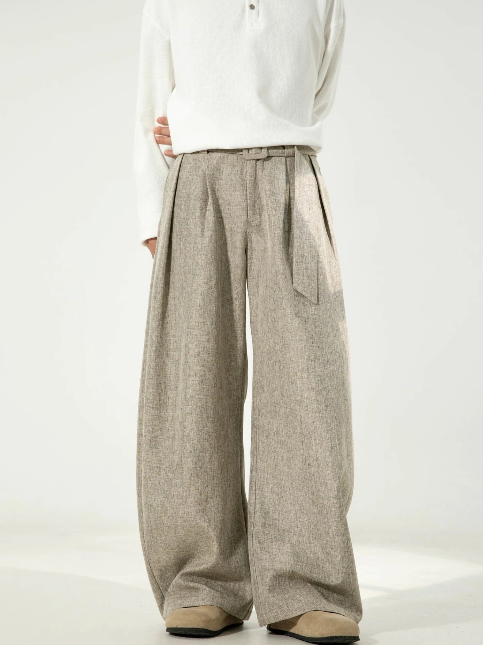 Male model wearing light beige linen-texture wide-leg curve trousers with front pleats and a matching removable belt in a minimalist studio