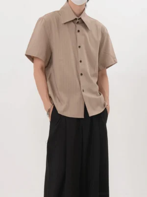 Khaki Acubi pinstripe short sleeve shirt shown from a front three quarter angle with pointed collar curved hem and black wide leg trousers