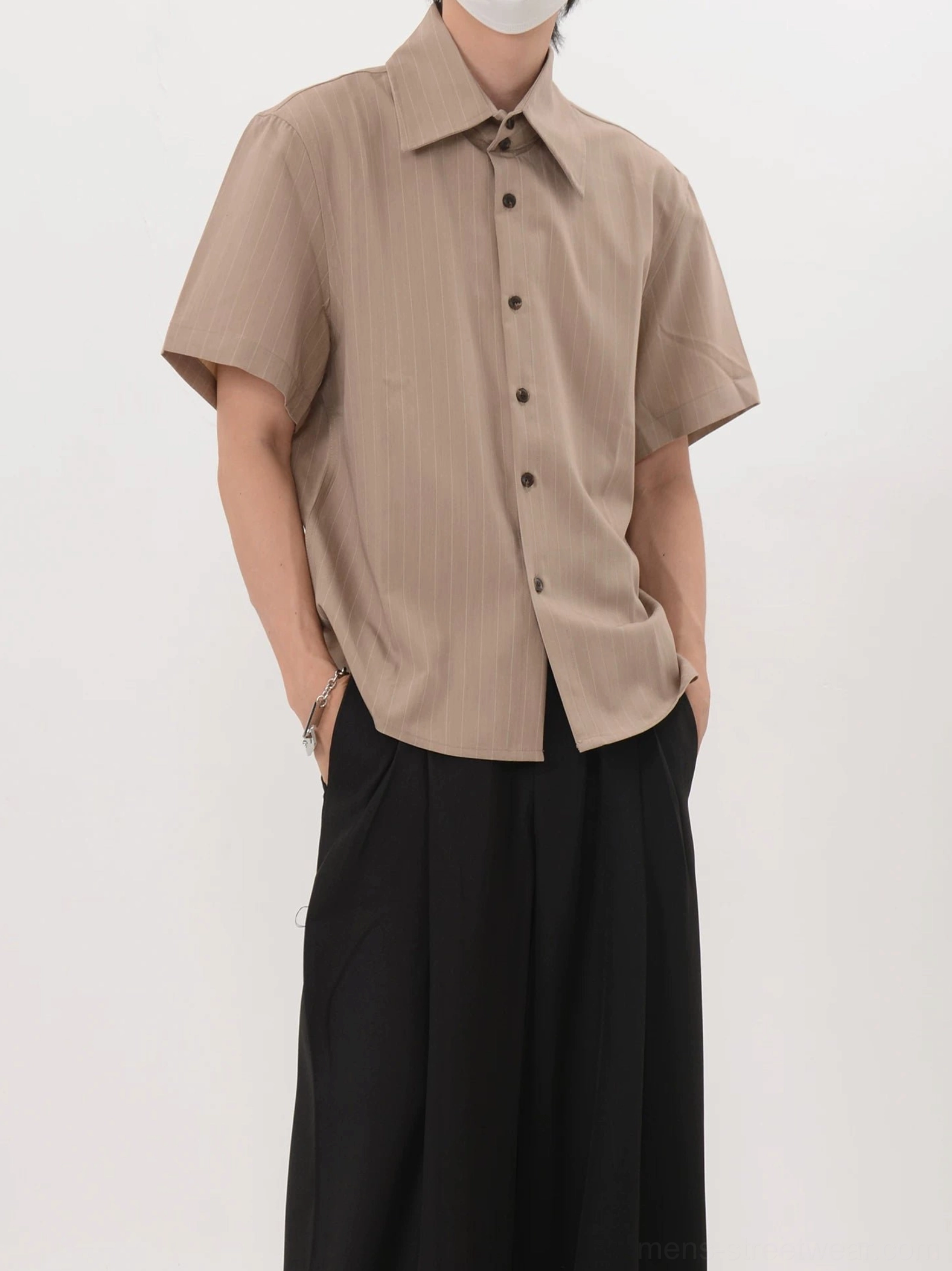 Khaki Acubi pinstripe short sleeve shirt shown from a front three quarter angle with pointed collar curved hem and black wide leg trousers
