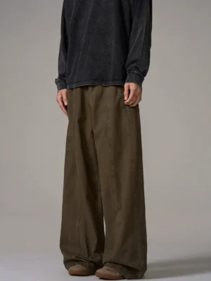 Front full-body male model wearing brown wide-leg cotton trousers with central front seam and relaxed Korean streetwear fit on grey studio background