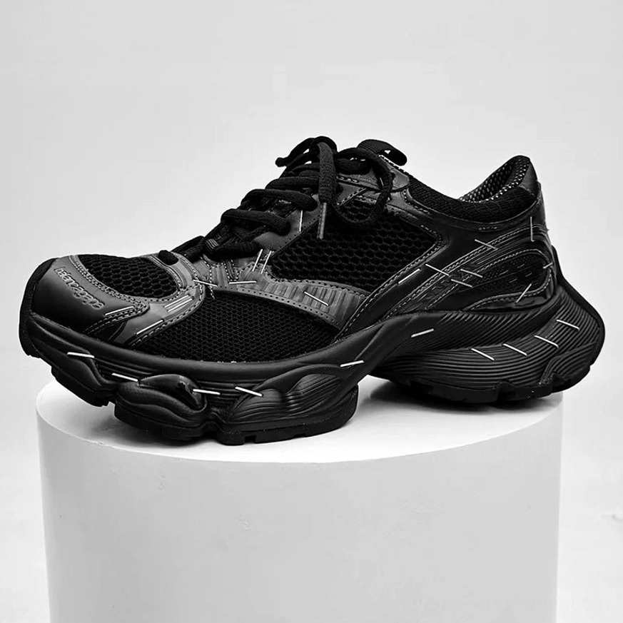 All-black chunky dad sneakers displayed from an angled front-side view with matte finish, stitch detailing, mesh construction, and heavy traction sole