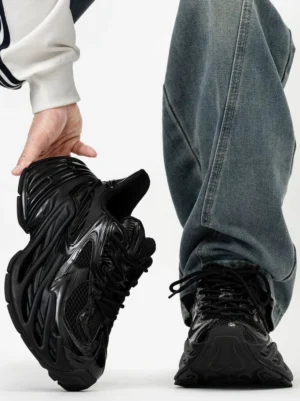 All-black futuristic chunky platform sneakers with glossy ridged overlays, breathable mesh panels, exaggerated wave-textured outsole, and approximately 11 cm height boost styled with baggy blue jeans