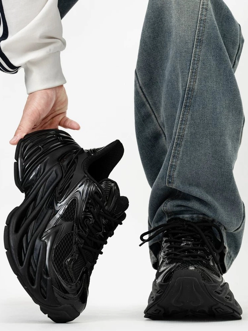 All-black futuristic chunky platform sneakers with glossy ridged overlays, breathable mesh panels, exaggerated wave-textured outsole, and approximately 11 cm height boost styled with baggy blue jeans