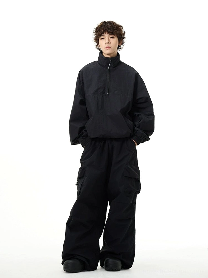 Full-body front view of an all-black oversized techwear windbreaker and wide-leg cargo pants streetwear set on a male model