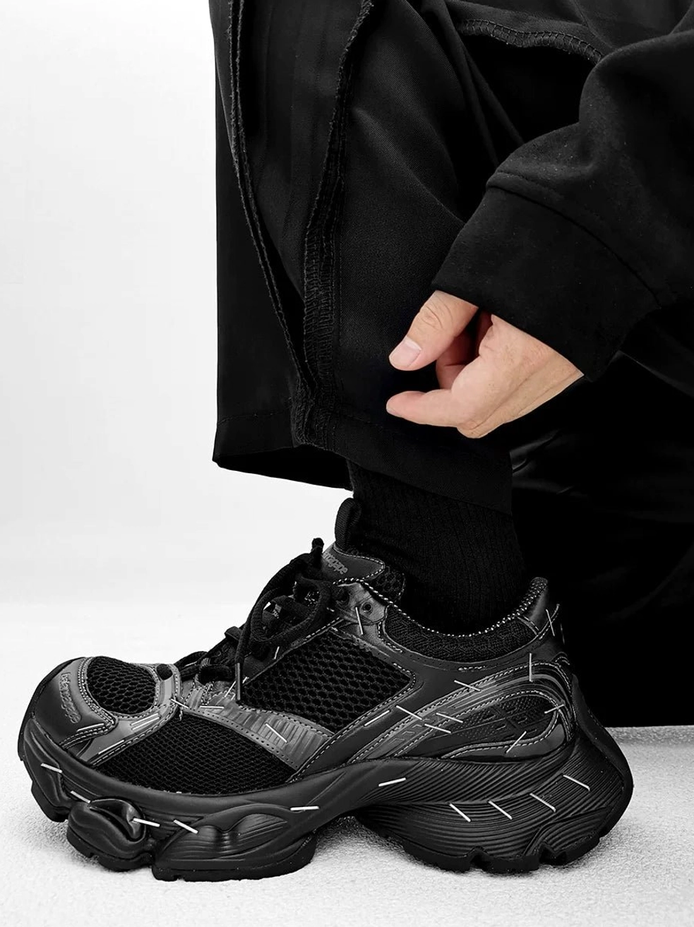 All-black retro chunky sneakers shown close up with decorative vamp stitching, mixed mesh panels, synthetic overlays, and deep tread outsole