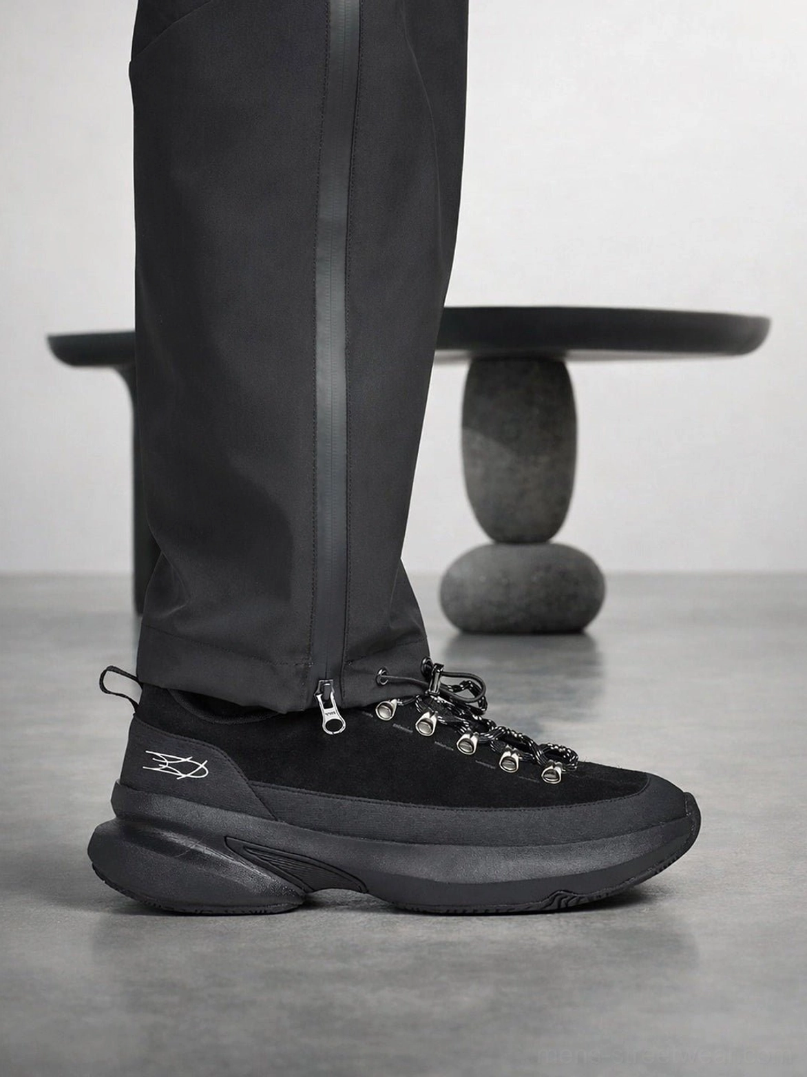 Side view of all-black samurai-inspired casual sneakers showing the textured toe cap, metal lace buckles, heel pull loop, and substantial urban outsole