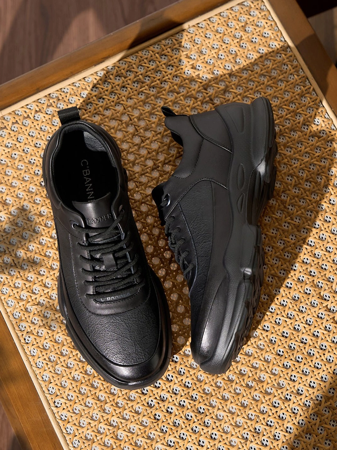 Top view of pair of all-black sculpted sole chunky sneakers showing textured leather-look panels and thick sole