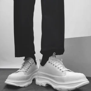 All-white chunky platform canvas sneakers worn with black formal trousers showing the thick rugged rubber sole