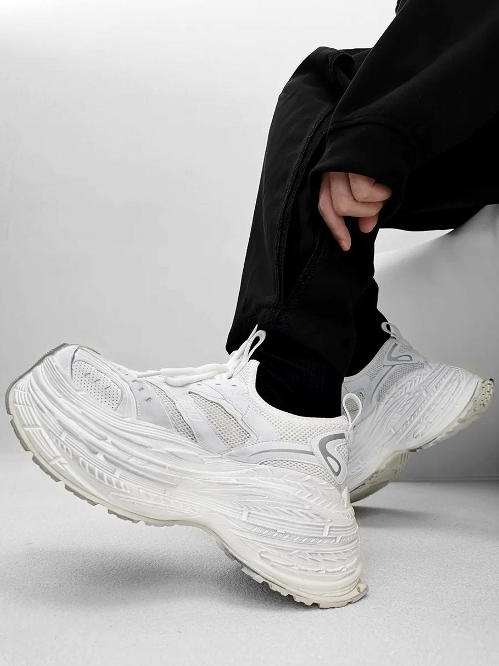 All white chunky platform dad sneakers with breathable mesh upper and layered textured sole worn with black streetwear pants