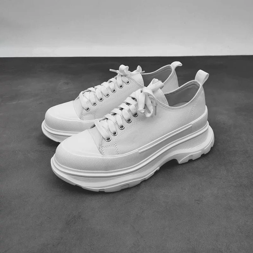 Pair of minimalist all-white low-top platform canvas sneakers with thick rugged rubber soles and heel pull tabs