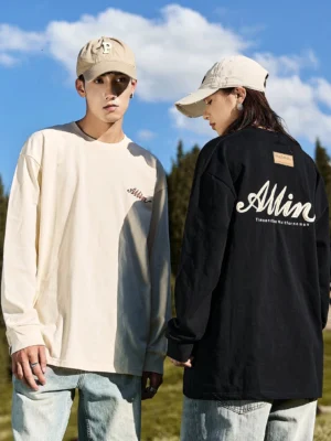 Couple wearing ivory white and black alpine script back graphic oversized cotton long sleeve streetwear tees outdoors