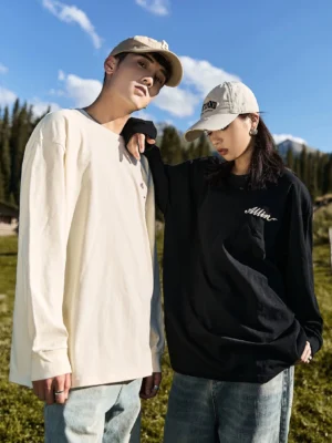 Matching black and ivory alpine script graphic long sleeve streetwear tees worn by couple in alpine forest setting