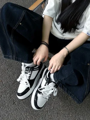 Anime cat graphic low-top sneakers worn with baggy dark jeans and a striped shirt on outdoor pavement