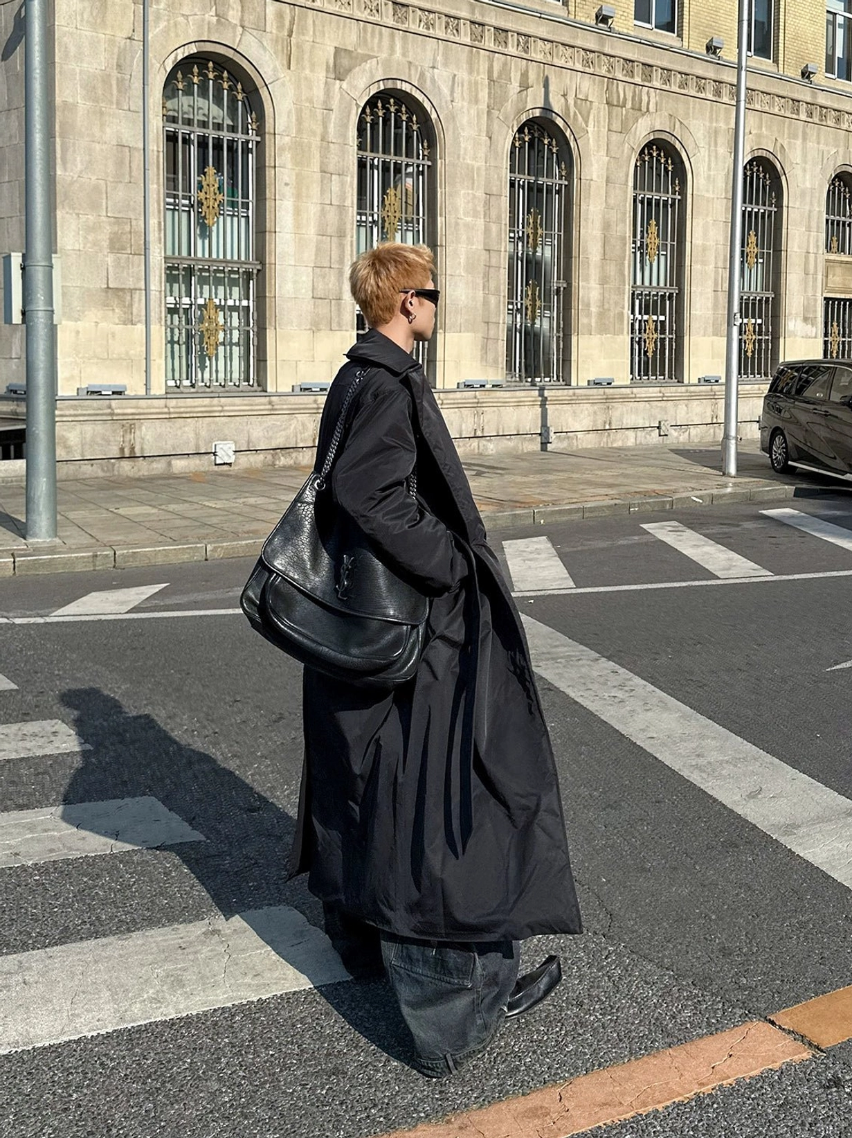 Back view of an ankle length oversized black belted overcoat featuring clean solid fabric side hem slits and relaxed urban streetwear fit