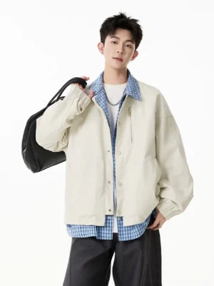 Apricot checker collar layered coach jacket for men styled with wide-leg trousers and black shoulder bag front view