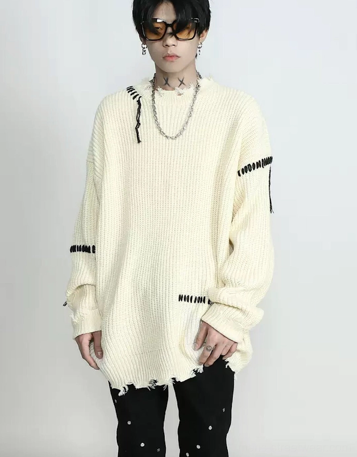 Front view of an apricot cream oversized knit sweater with black contrast stitching, distressed sleeve details, drop shoulders, and a raw frayed hem