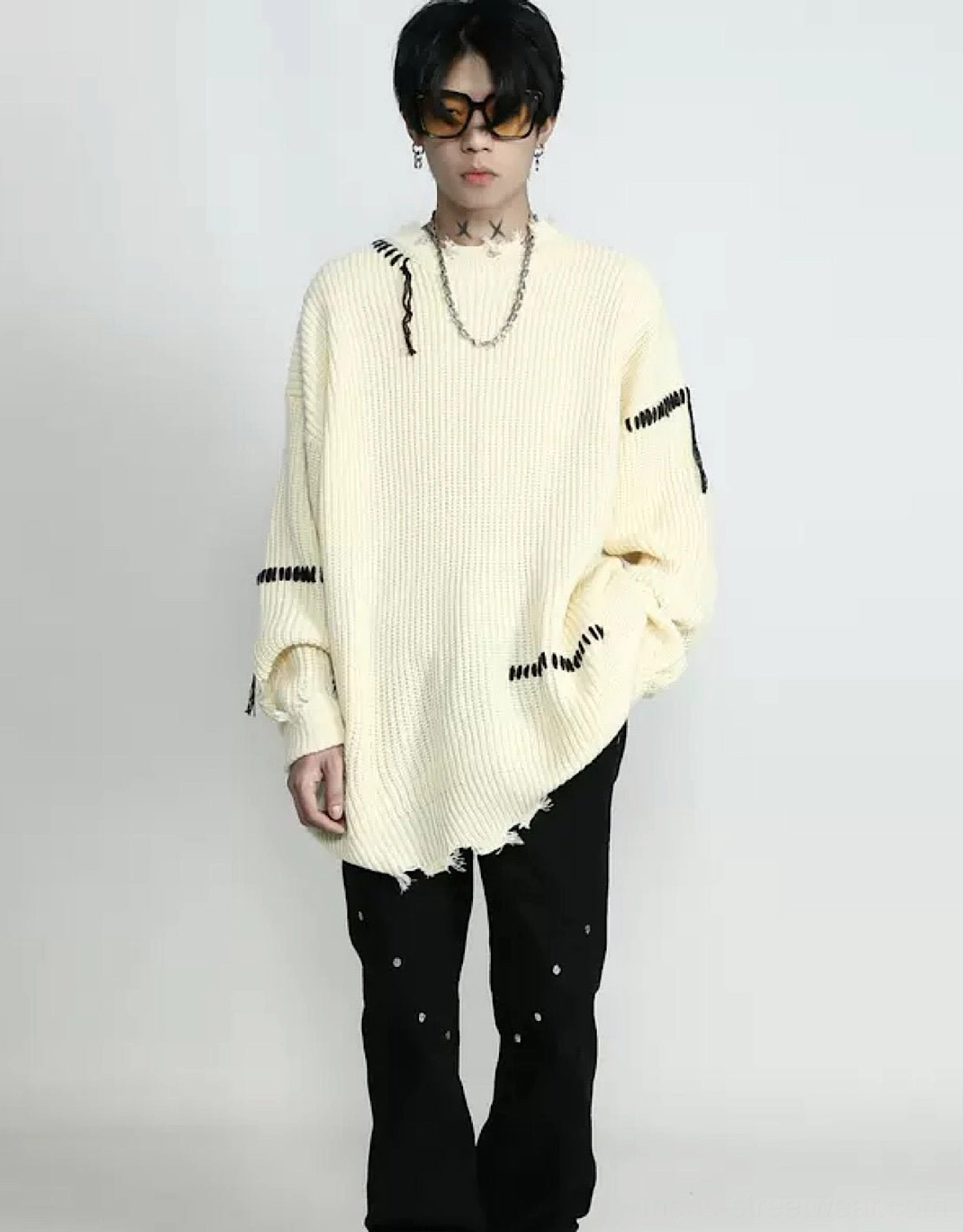 Front styling view of an apricot distressed oversized sweater with black stitched patches, relaxed sleeves, ribbed texture, and raw uneven hemline