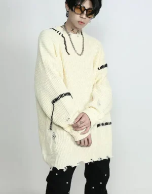 Apricot distressed stitched oversized knit sweater shown from a three-quarter side view with black whipstitch details, frayed hem, and layered silver streetwear jewelry