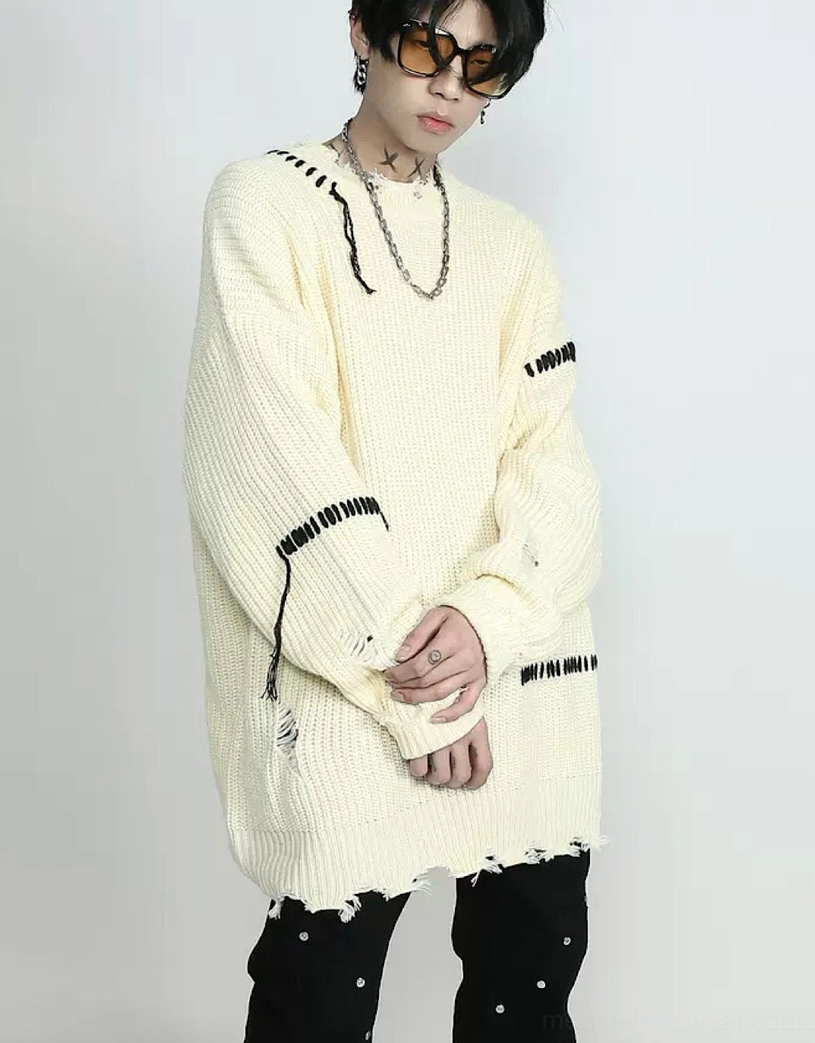 Apricot distressed stitched oversized knit sweater shown from a three-quarter side view with black whipstitch details, frayed hem, and layered silver streetwear jewelry