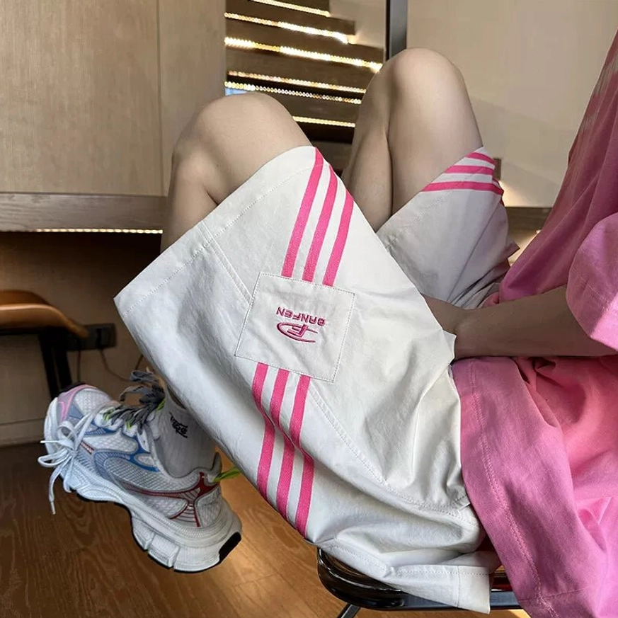 Apricot loose-fit Asian streetwear shorts with hot pink three-stripe side trims, oversized pink tee, and colorful chunky sneakers
