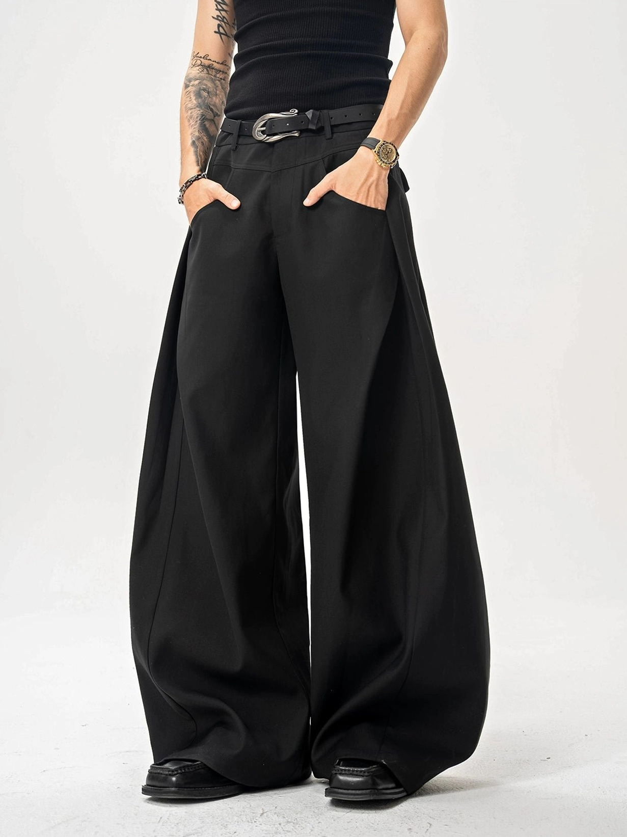Black ultra wide-leg men's trousers showing deep side pleats, oversized silhouette, and leather dress shoe styling