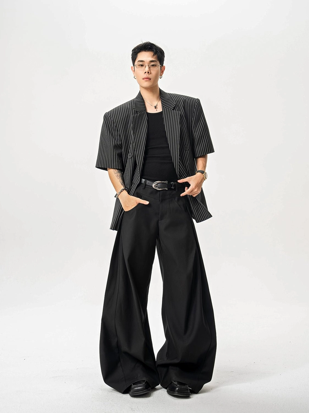 Black tailored ultra wide-leg trousers styled with striped short-sleeve blazer, tank top, belt, and leather shoes