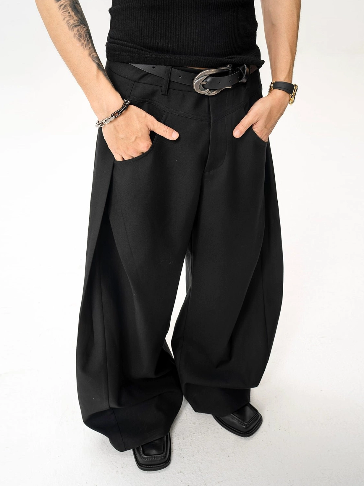 Front lower-body close-up of black architectural wide-leg tailored trousers with silver buckle leather belt