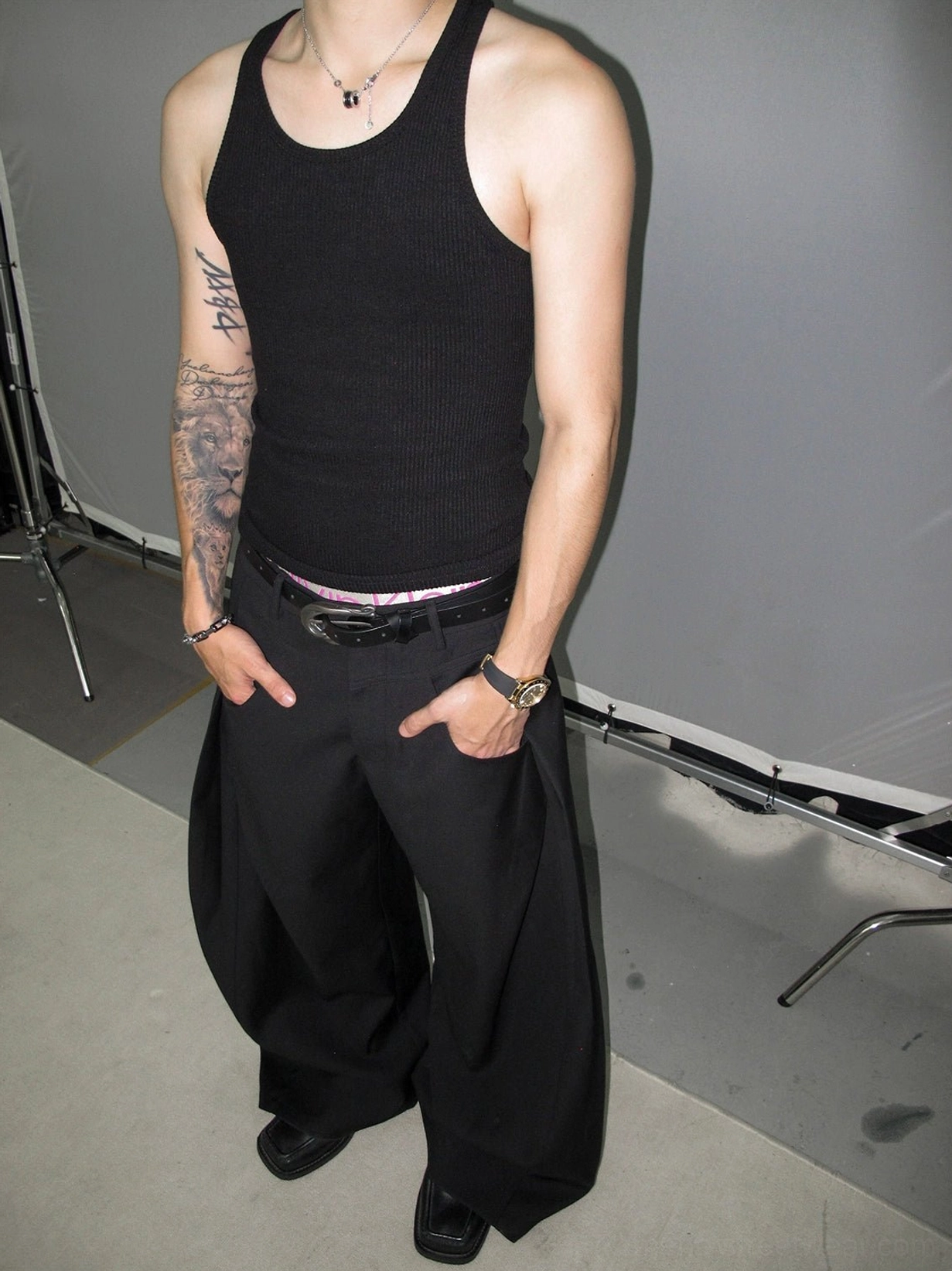 Close-up of black wide-leg trousers waistband with leather belt, silver hardware, pleats, and matte twill texture