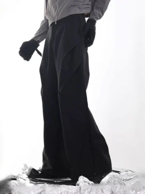 Black architectural wide-leg panel trousers shown from a low side profile with asymmetrical diagonal seams and a tailored streetwear waistband