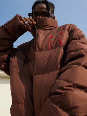 Brown oversized duck-down puffer jacket close-up showing high stand collar quilted texture and embroidered streetwear detail