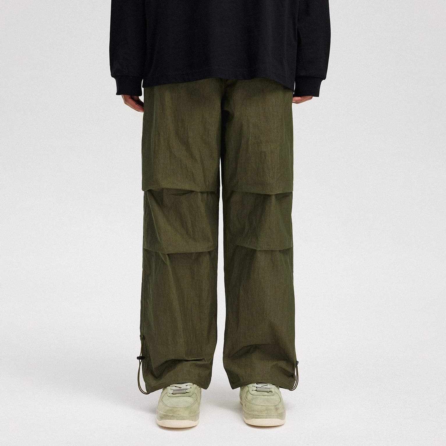 Army green crinkled wide-leg track pants shown from the back with pleated knees and adjustable ankle drawstrings
