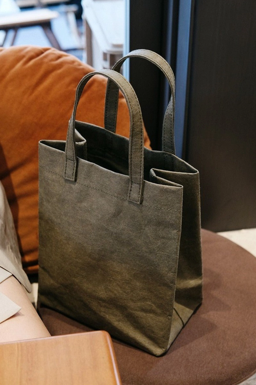 Army green vintage kraft paper texture cotton tote bag displayed on a brown round stool with matching soft handles