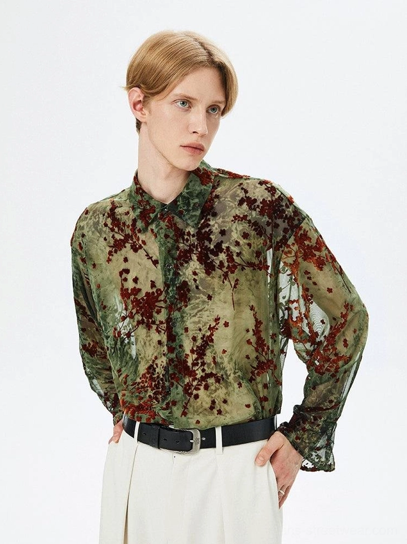 Male model wearing an army green semi-sheer floral button-up shirt with dark red botanical print in a front three-quarter studio view