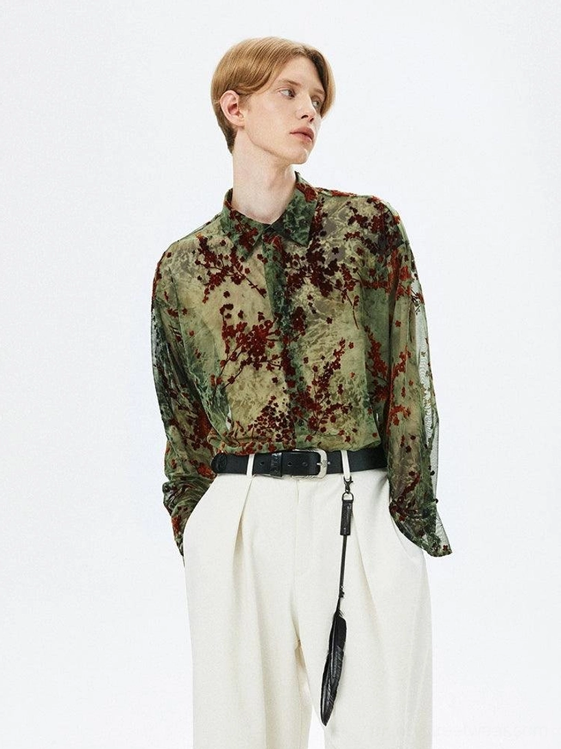 Front view of men's army green sheer floral long-sleeve button-up shirt styled with white wide-leg trousers and black belt