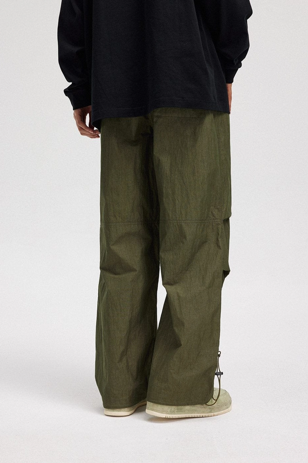Army green wide-leg drawstring track pants shown from the rear side with relaxed streetwear proportions