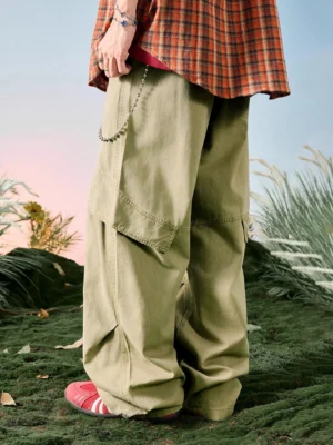 Army khaki origami panel wide leg cargo pants shown from the rear three quarter view with oversized side pocket, drawstring waist, decorative chain, plaid shirt, and red sneakers