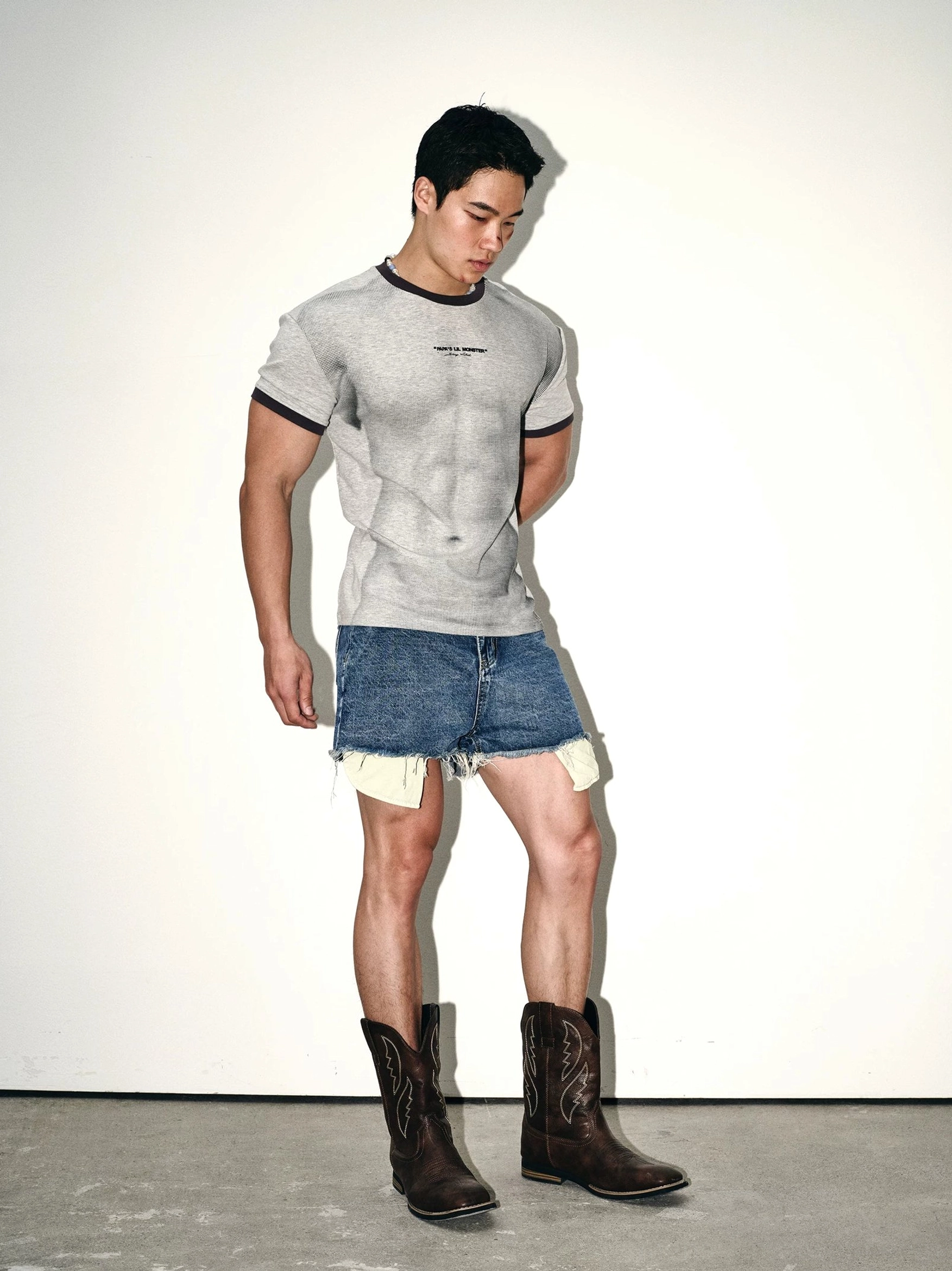 Ash gray contrast ringer tee styled with frayed denim shorts and brown cowboy boots in a full body side profile streetwear outfit