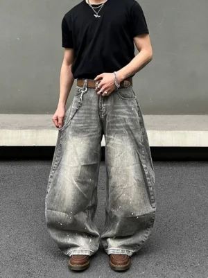 Front full-body view of ash gray paint-splatter balloon jeans with oversized wide legs, acid washed denim, black T-shirt, brown leather belt, wallet chain, and work boots