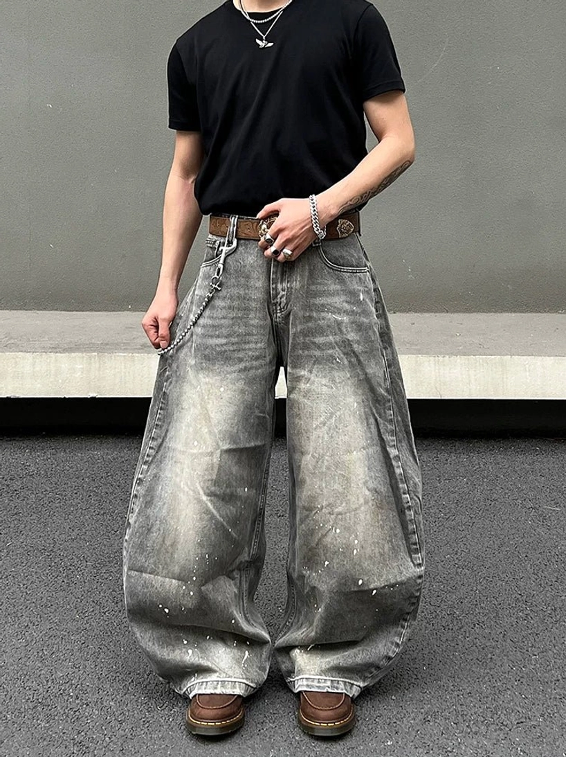 Front full-body view of ash gray paint-splatter balloon jeans with oversized wide legs, acid washed denim, black T-shirt, brown leather belt, wallet chain, and work boots