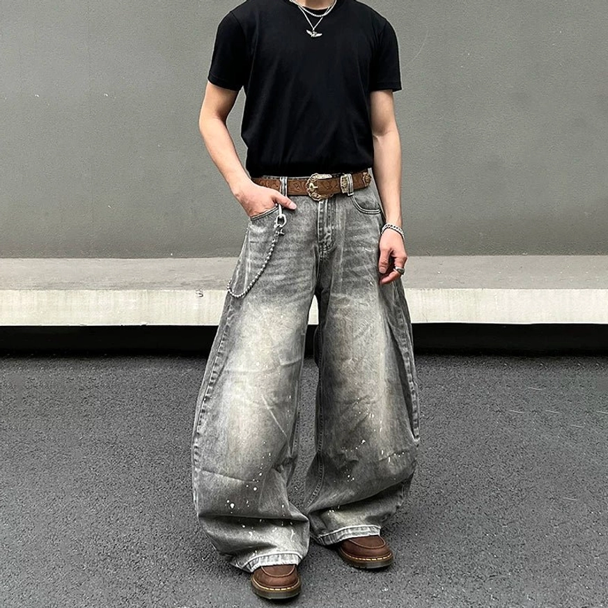 Casual front view of ash gray wide-leg paint-splatter jeans with extra loose balloon fit, faded washed denim, black T-shirt, brown belt, wallet chain, and work boots