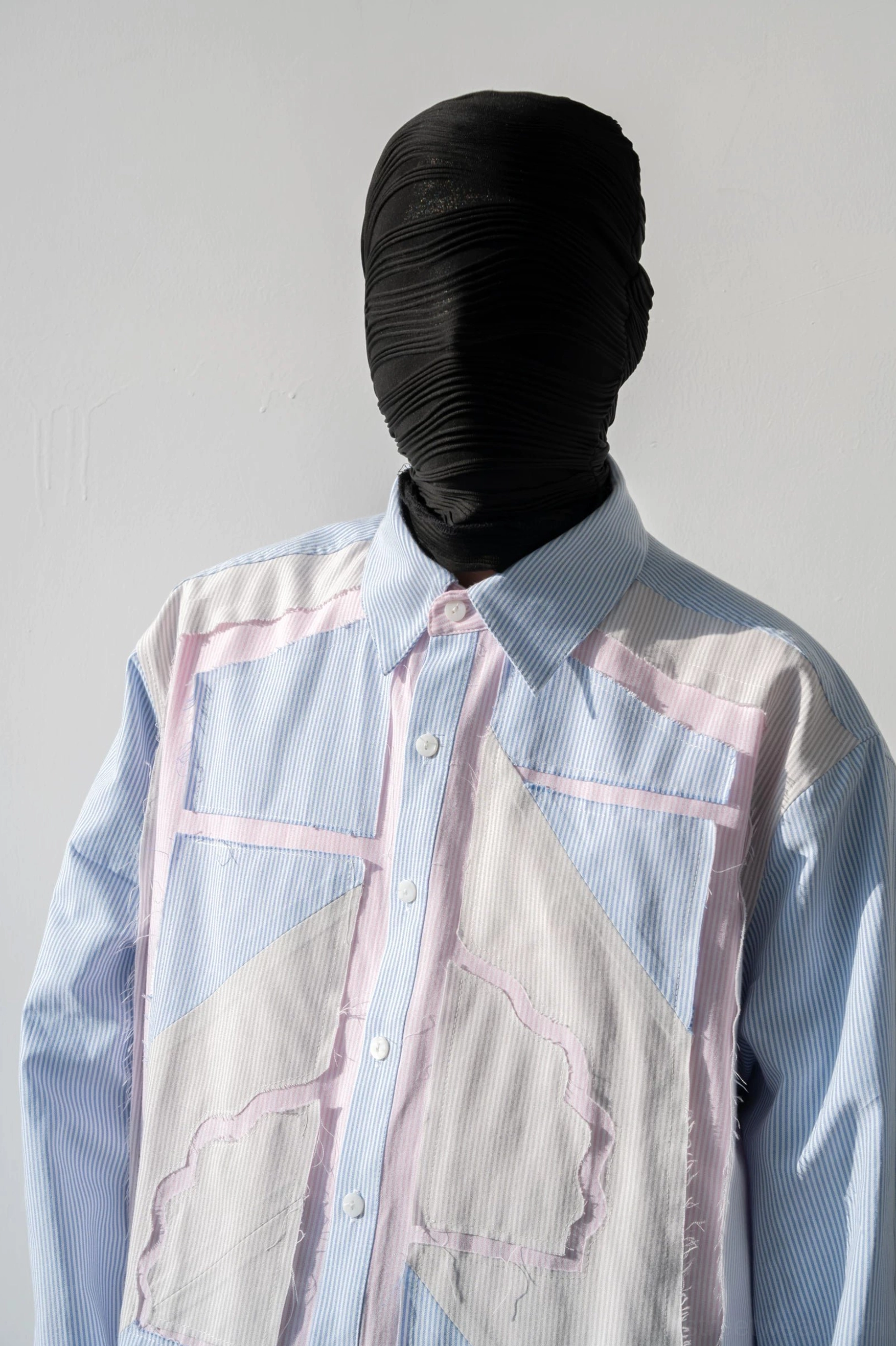 Close-up front view of asymmetric blue and white geometric patchwork shirt with pastel pink edging